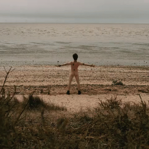 there is a boy standing on the beach holding his arms out