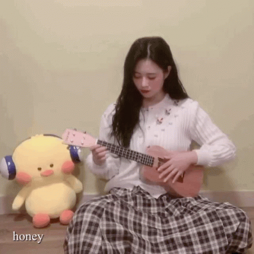 girl playing a blue ukulele beside a stuffed toy