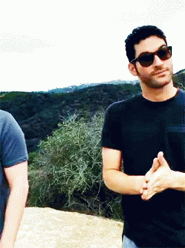 two young men, one with sunglasses and one without, are standing on a rock - covered hillside