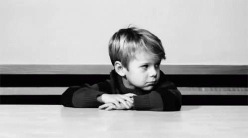 a young child sitting at a table with his arms folded up