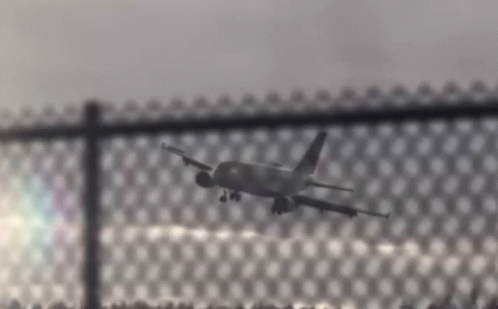 a plane flying through the air and behind a fence