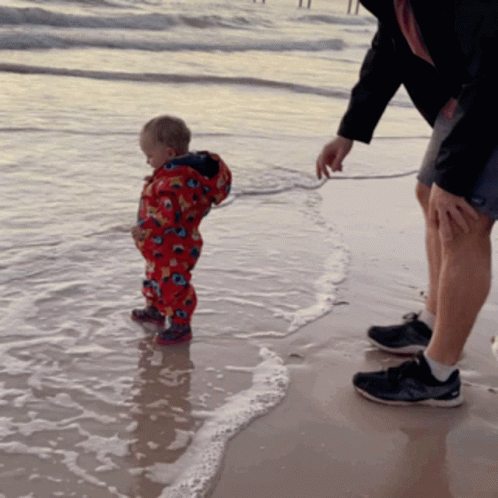 a man holding a child's hand while standing on the beach