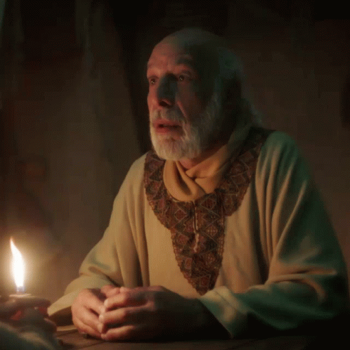 an older man holding a lit candle sitting at a desk
