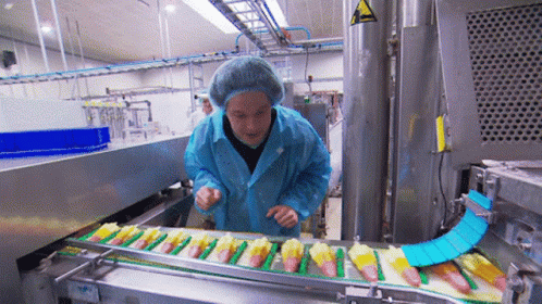 the man wearing a yellow coat stands over a conveyor belt holding packages