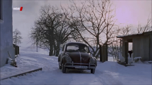 an old car on a snowy road near buildings