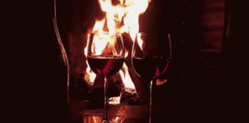 wine glasses being held with two forks in front of a burning fireplace