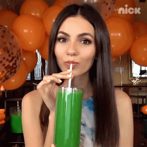 a young woman wearing blue hair drinking a green drink