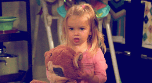 a little girl holding a teddy bear on top of a table