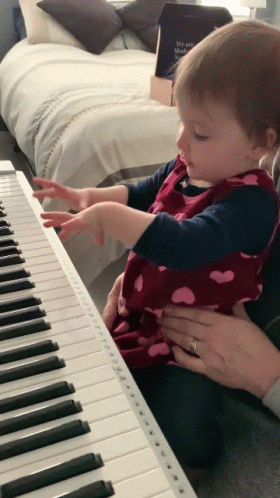 a small child plays with her dad as they sit by the piano