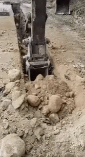 a large machine digging through the rocks on a dirt road