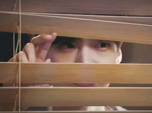 a man is peeking out from behind the blinds