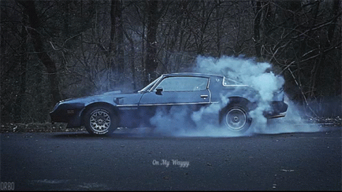 an old school car makes a smoke trail on the road