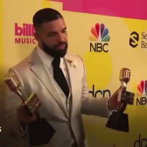 the man is holding several award trophies while giving a speech