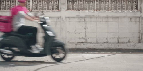a person on a moped drives by an old building