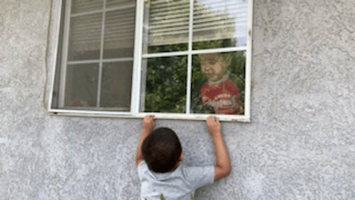 a young child hanging out a window with his arms