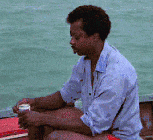a man in tan shirt sitting on wooden boat next to water