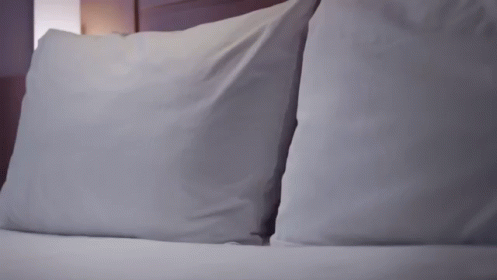 a white bed topped with two pillow cases next to a night stand
