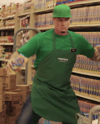 a person dressed as a man in a green apron and hat standing in front of a rack of beverages