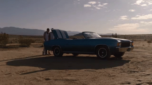 two people are standing near an old car in the desert