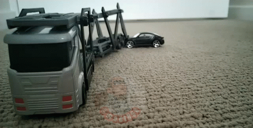toy cars are on a carpeted floor near the vehicle