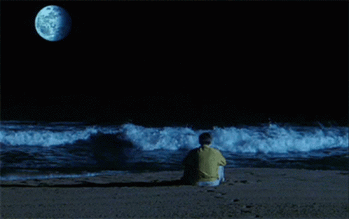a man sits at the edge of a beach watching waves