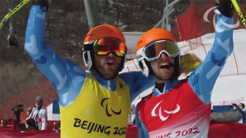 the two skiers in blue vests hold their ski poles