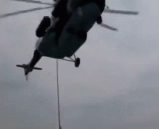 a helicopter with an extra wing being hoisted by ropes