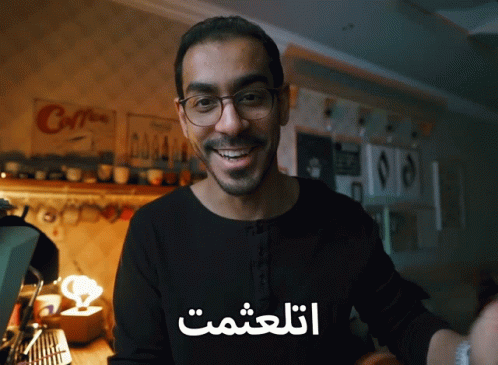 a man with glasses smiling and wearing a t - shirt that says in arabic