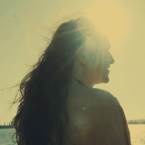 woman with long flowing hair on beach looking out at water