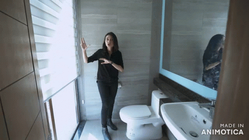 a woman in a restroom with one hand up and another on a toilet