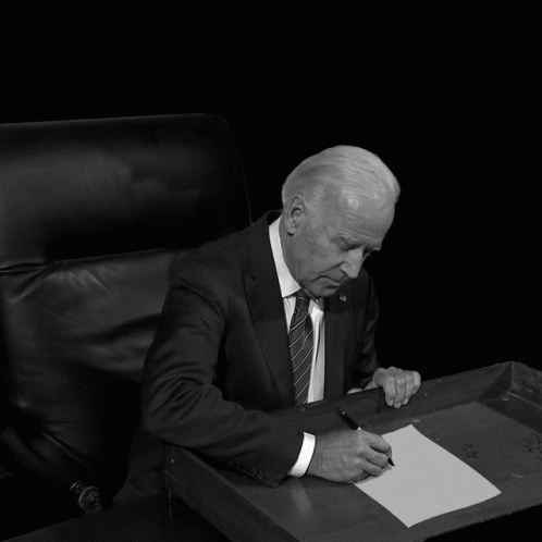 an older man in a suit sits at a desk
