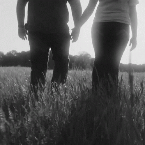 two people are holding hands standing in the middle of a field