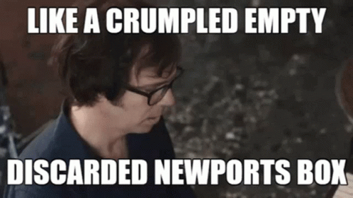 a  sitting in front of a sign that says like a crumpled empty discarded newports box