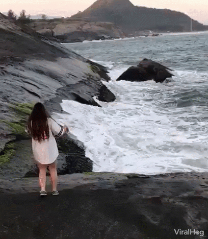 a woman is on the rocks looking at waves