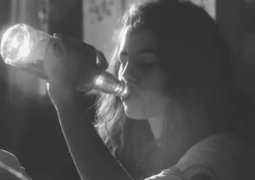 a woman drinking soing from a bottle in black and white