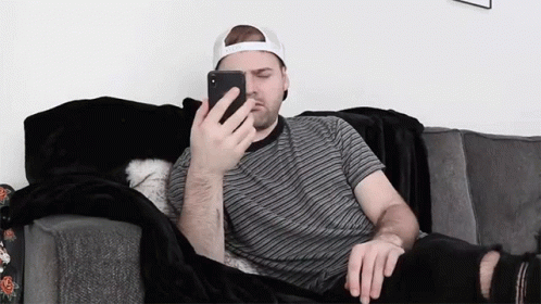 a man sits on the couch while looking at his cell phone