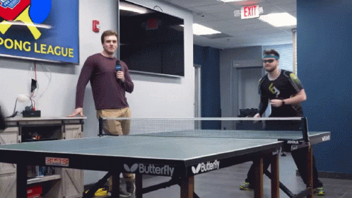 a couple of guys standing around a ping pong table