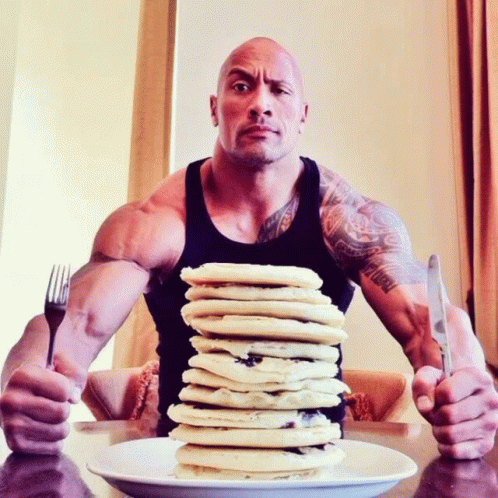 a bald man with his arms crossed and a plate full of pancakes on his lap