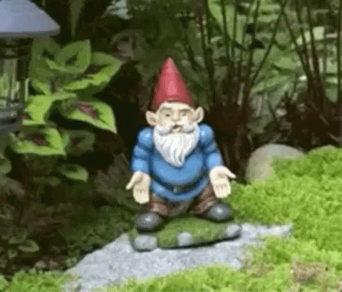 a gnome statue sitting in the grass in the garden