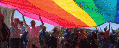 there are many people that are standing under a colorful kite
