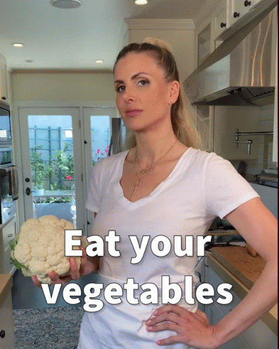an attractive young woman standing in a kitchen with the caption eat your vegetables