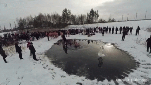 the people are standing near a small pool in the snow
