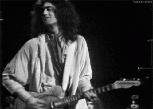 a man with long hair playing a guitar on stage