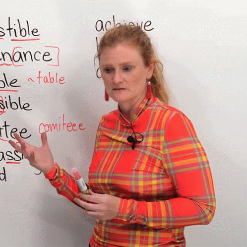 a woman wearing blue and white writing on a whiteboard