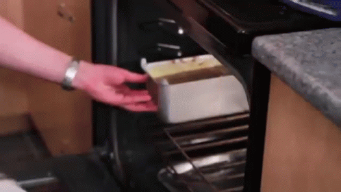 person with purple gloves taking food out of an oven