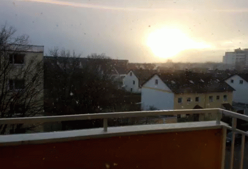 the sun is in the distance above houses on the roof of a building
