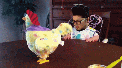 an artificial chicken and a man face each other at a table