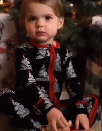 this little girl is sitting in front of a christmas tree