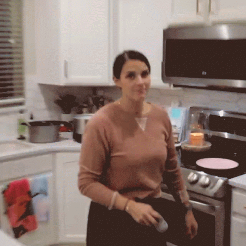 a woman with dark hair is standing in a kitchen