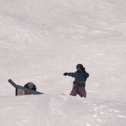 a man wearing a helmet stands next to a snowboard that fell down a slope